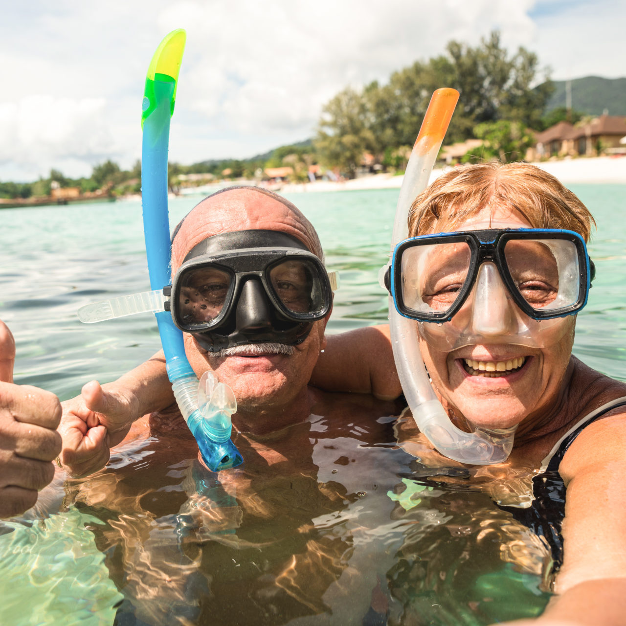 Senior happy couple taking selfie in tropical sea excursion with water camera - Boat trip snorkeling in exotic scenarios - Active retired elderly and fun concept around the world - Warm bright filter