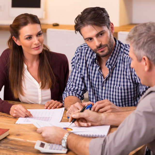 Businessman explaining loan policy to young couple. Happy young couple discussing with a financial agent their new investment. Financial consultant presents bank investments to a young couple.