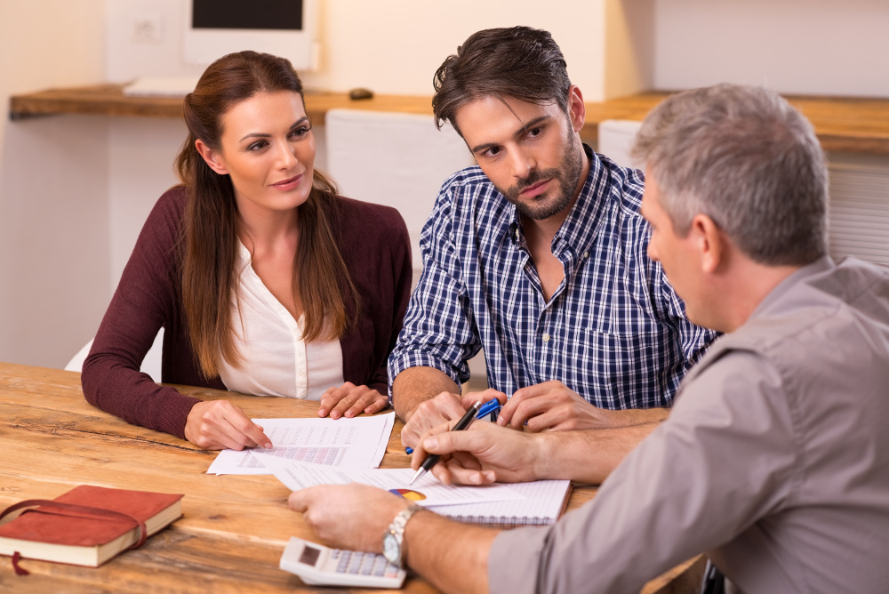 Businessman explaining loan policy to young couple. Happy young couple discussing with a financial agent their new investment. Financial consultant presents bank investments to a young couple.